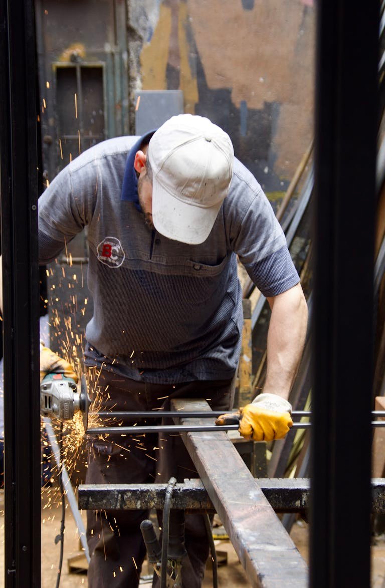 A worker in a workshop uses a grinder on metal with bright sparks everywhere.